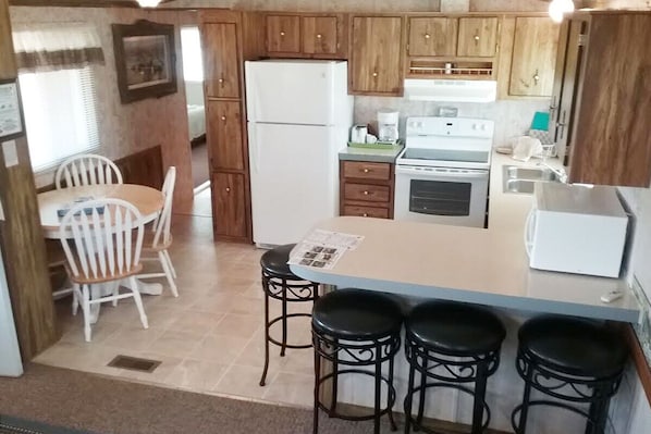 Une cuisine compacte avec des meubles en bois, un réfrigérateur blanc, une cuisinière et un petit coin repas comprenant une table et des chaises.