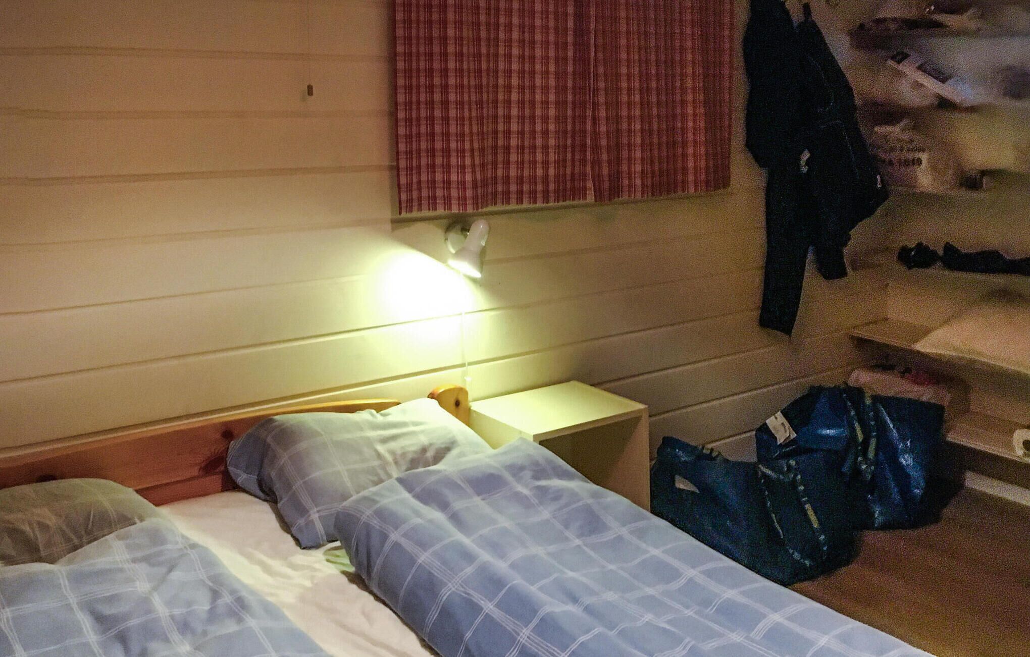 Una habitación pequeña y tenue con una cama individual, una mesita de noche y un bolso en el suelo.