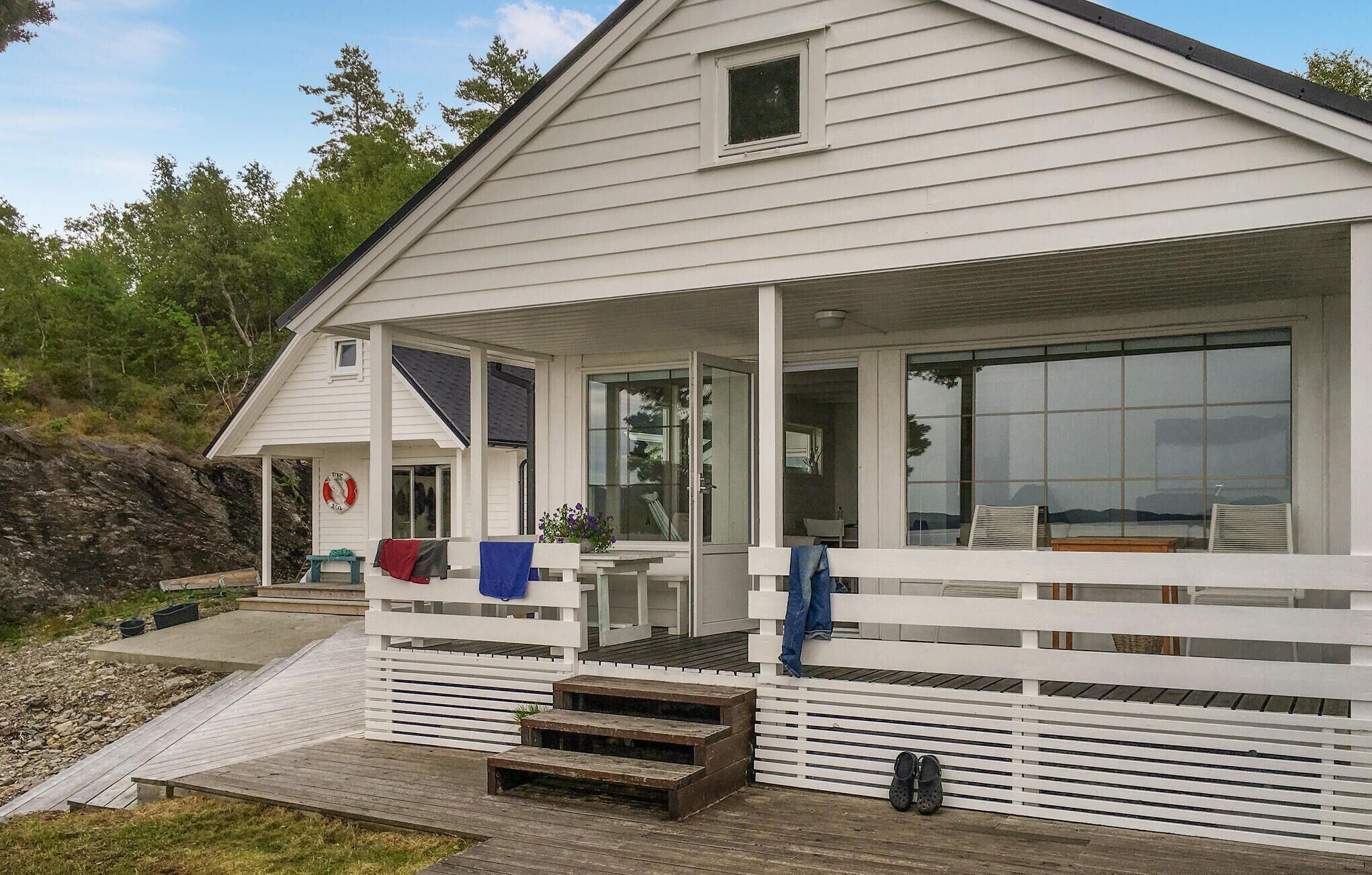 A white house with a covered porch, a small deck, and a lifebuoy on the wall.