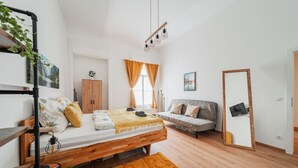 A modern bedroom with a wooden bed, a sofa, a mirror, and a TV. - 3 Bedrooms - 74sqm - 10 Min. Inner City (Vienna)