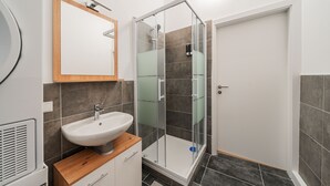 A modern bathroom with a glass-enclosed shower, a wooden vanity with a sink, and a mirror above it. - 3 Bedrooms - 74sqm - 10 Min. Inner City (Vienna)