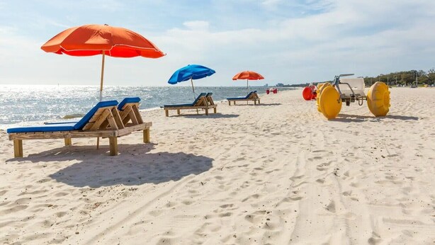 A beach with sun loungers and umbrellas, a lifeguard stand, and a yellow beach buggy. - Beach house, 1.5 blocks from beach, 3bd, 3 bath (gulfport)
