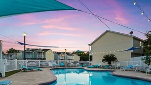 A swimming pool with lounge chairs and string lights, surrounded by a white fence and a building. - Beach house, 1.5 blocks from beach, 3bd, 3 bath (gulfport)