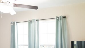 Une chambre à coucher avec un lit, un téléviseur posé sur un meuble en bois et un ventilateur de plafond.