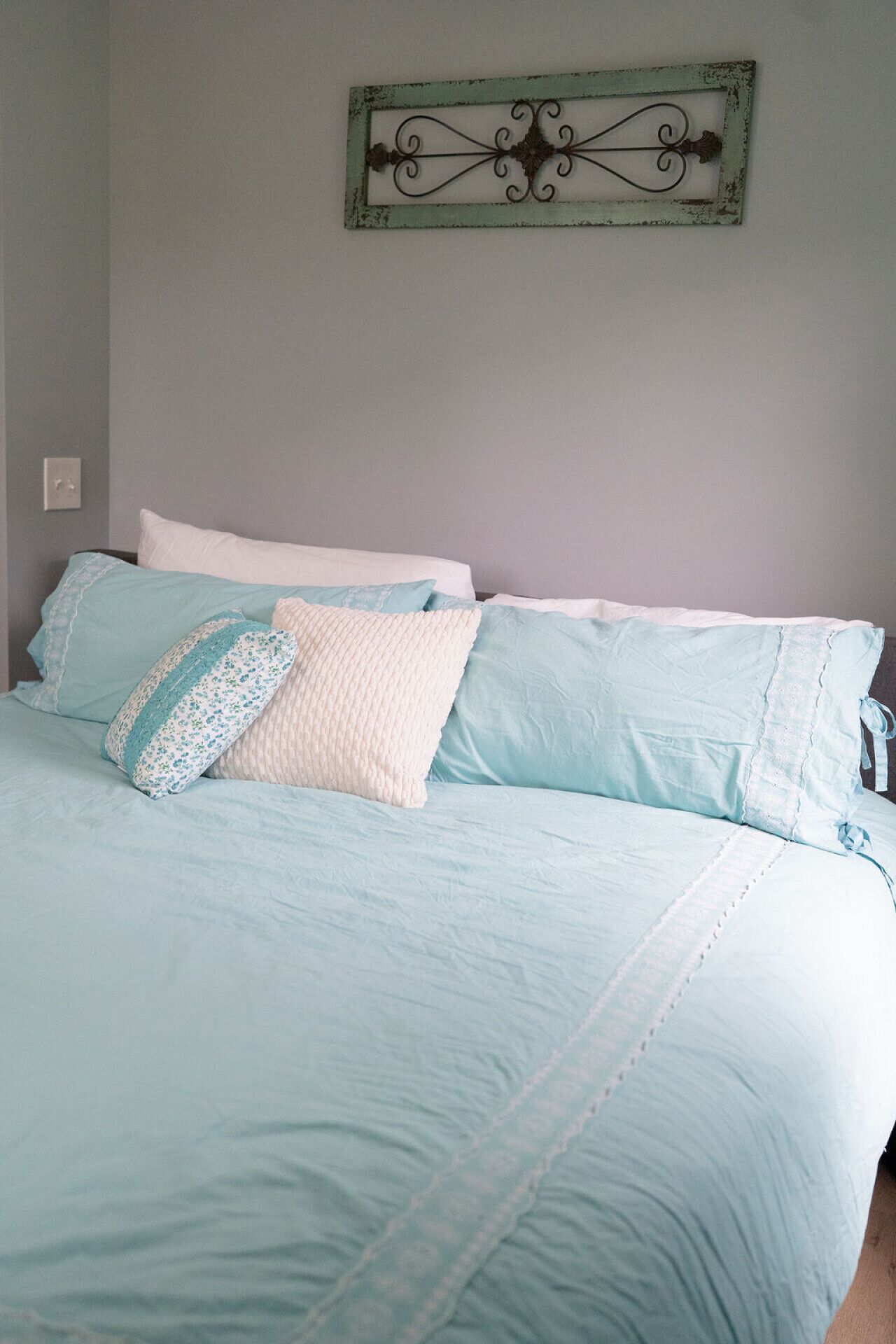 Quarto com cama, almofadas e um objeto decorativo na parede.
