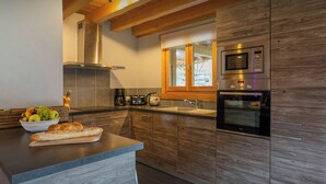 Een moderne keuken met houten kastjes, een ingebouwde oven en een groot eiland met een schaal fruit en brood.
