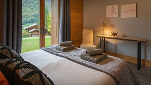 Een hotelkamer met een groot bed, een stoel, een bureau en uitzicht op een bebost gebied.
