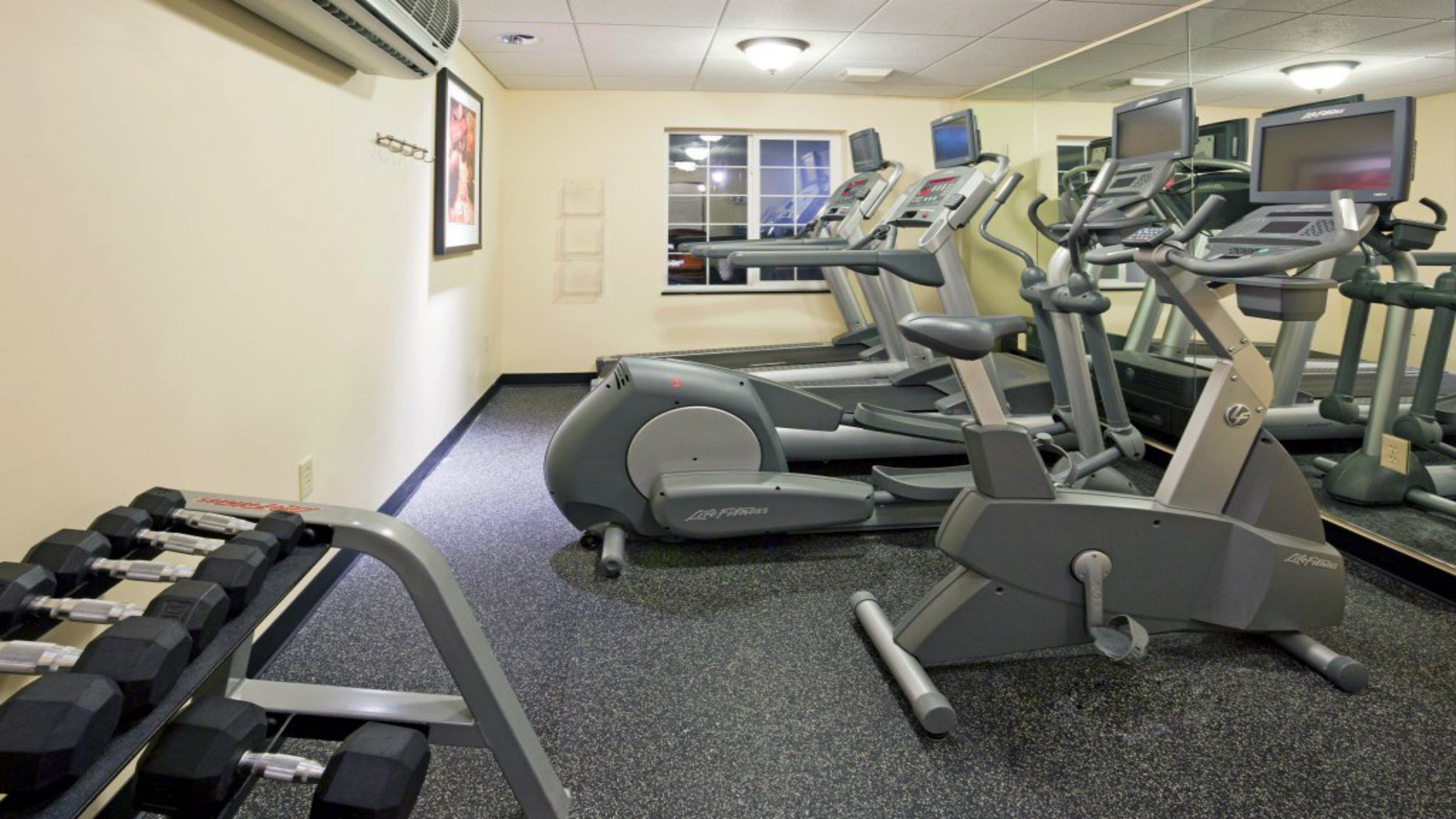 Une salle de sport équipée de tapis de course, de vélos elliptiques et d’un porte-haltères.