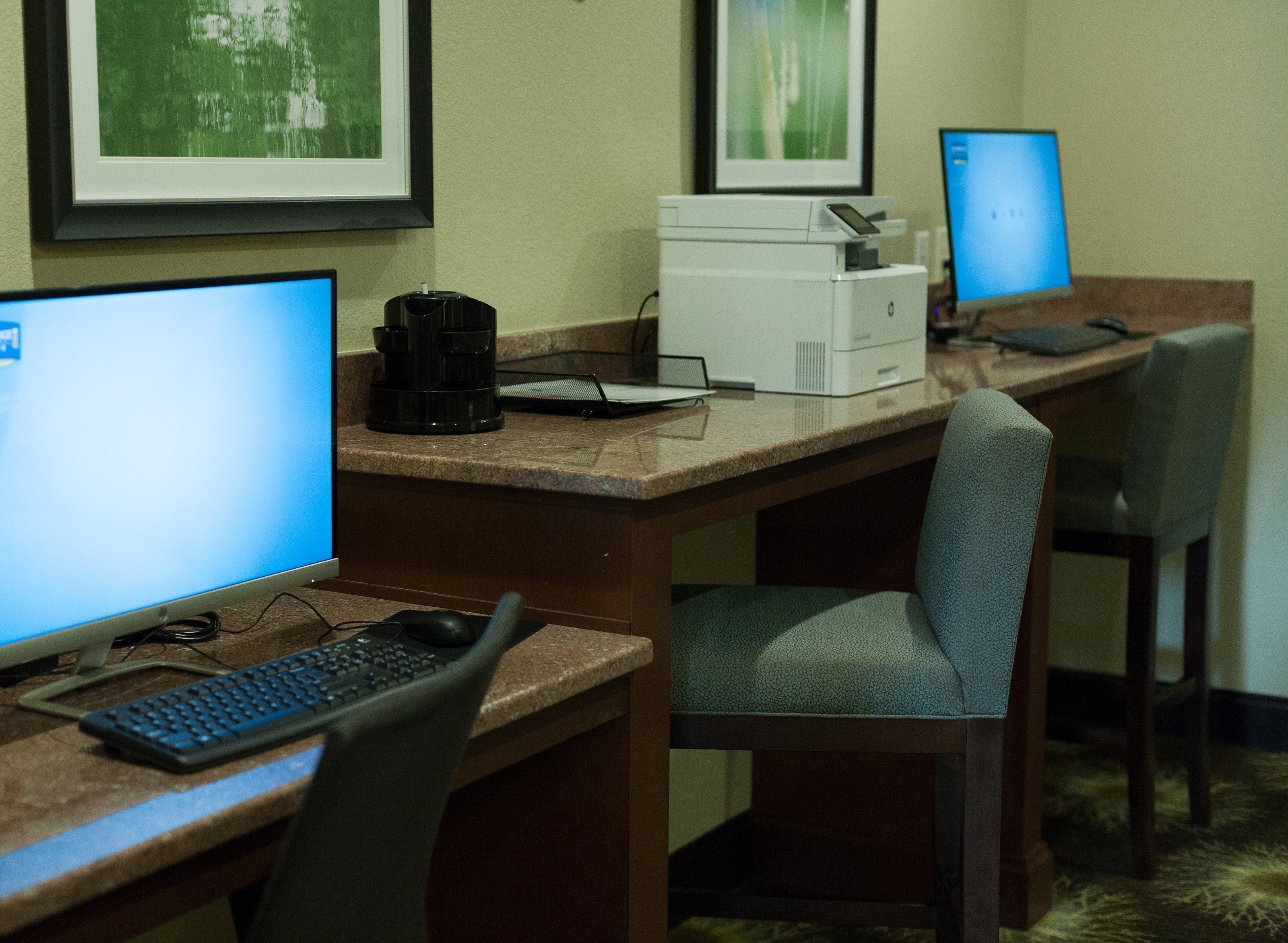 A hotel workspace with multiple computer desks, each equipped with a desktop computer, keyboard, and mouse.
