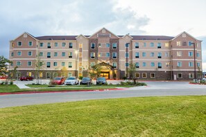 A multi-story hotel with a central entrance, parking lot, and a well-maintained lawn.