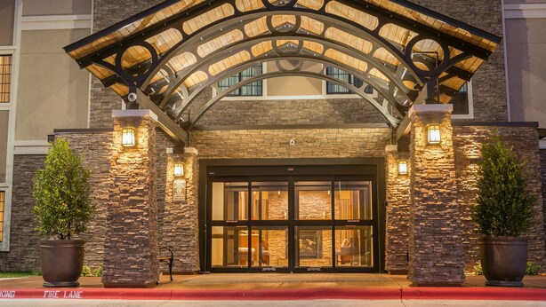 A hotel entrance with a stone facade, large glass doors, and a covered entrance area with lighting. - Close to TU | Modern Suite + Heated Outdoor Pool (Austin)