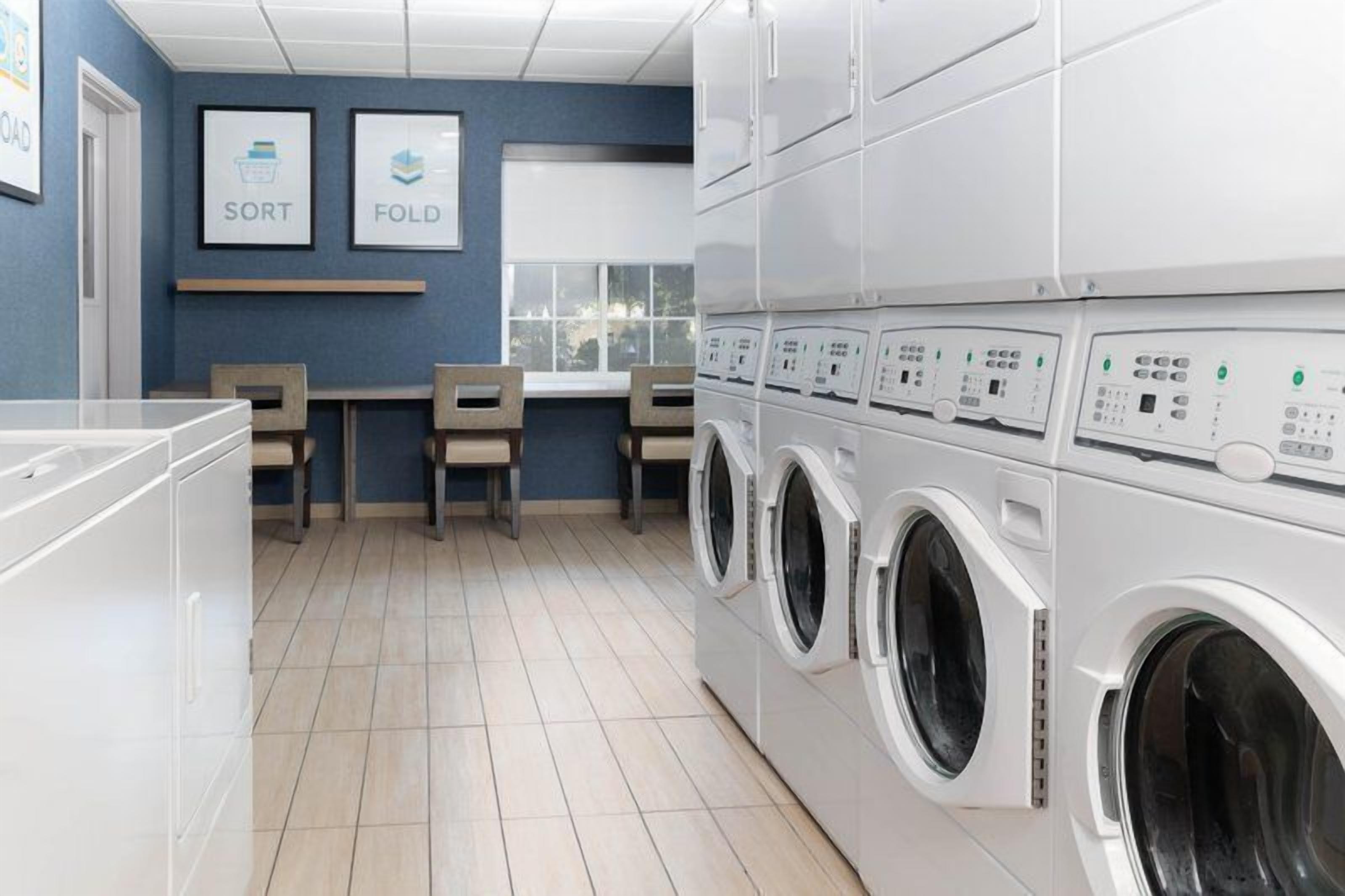 A laundry room with stacked washing machines, a sorting area, and a window.