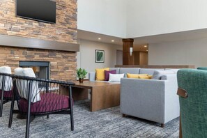 A modern lounge area with a stone wall, a flat-screen TV, a fireplace, and a seating arrangement including a sofa and chairs. - Amazing Central Location | Fitness Center + Pool (Chandler)