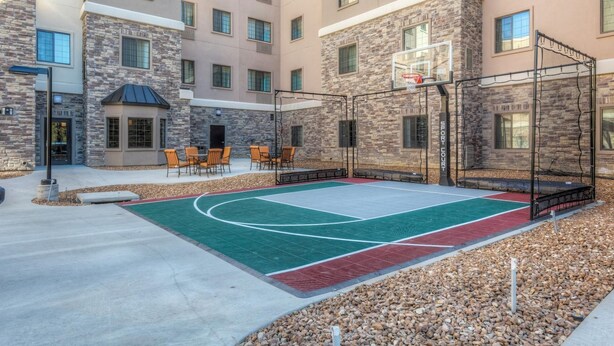 Ein Basketballplatz im Freien mit Netz, umgeben von Gebäuden aus Stein und Backstein, sowie Sitzmöglichkeiten im Freien.