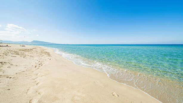 Une plage avec une eau d’un bleu limpide et un rivage sablonneux.