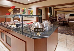 A buffet area with a sign indicating free daily breakfast, a glass display case, and a dining area with tables and chairs. - Accessible 2-BR Suite w/ Tub & 2 Bathrooms (Oconomowoc)