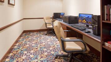 A conference room with three beige chairs, a desk with a computer, printer, and monitor, carpeted floor, and a bookshelf with books.