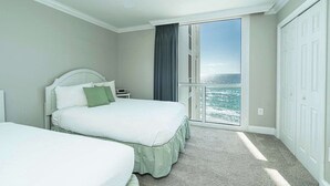 Quarto de hotel com cama, mesa de cabeceira, ventilador de teto, vista para o oceano e porta de correr para a varanda.