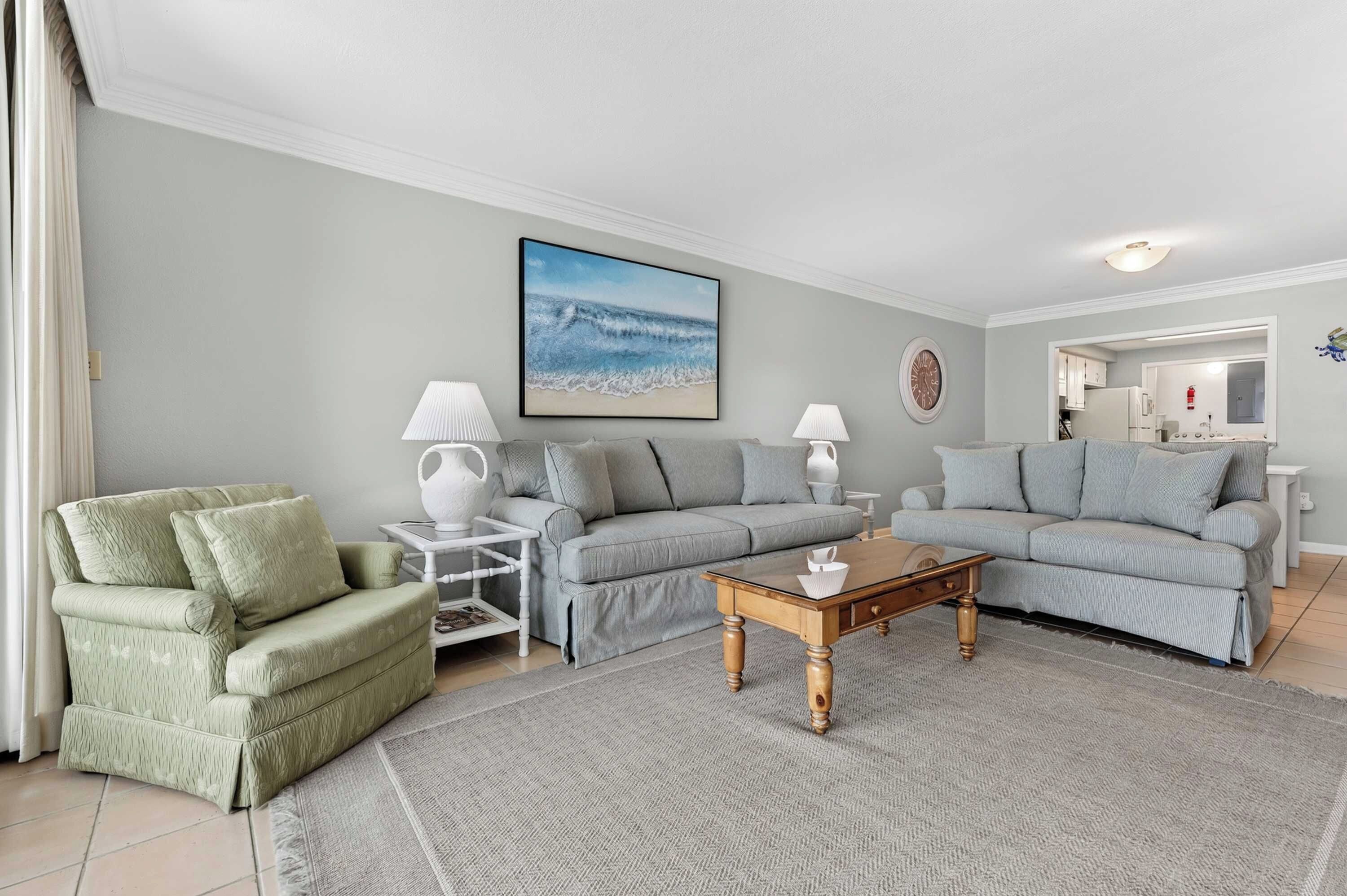 A living room with a grey sofa, a green armchair, a coffee table, and a painting of the ocean.