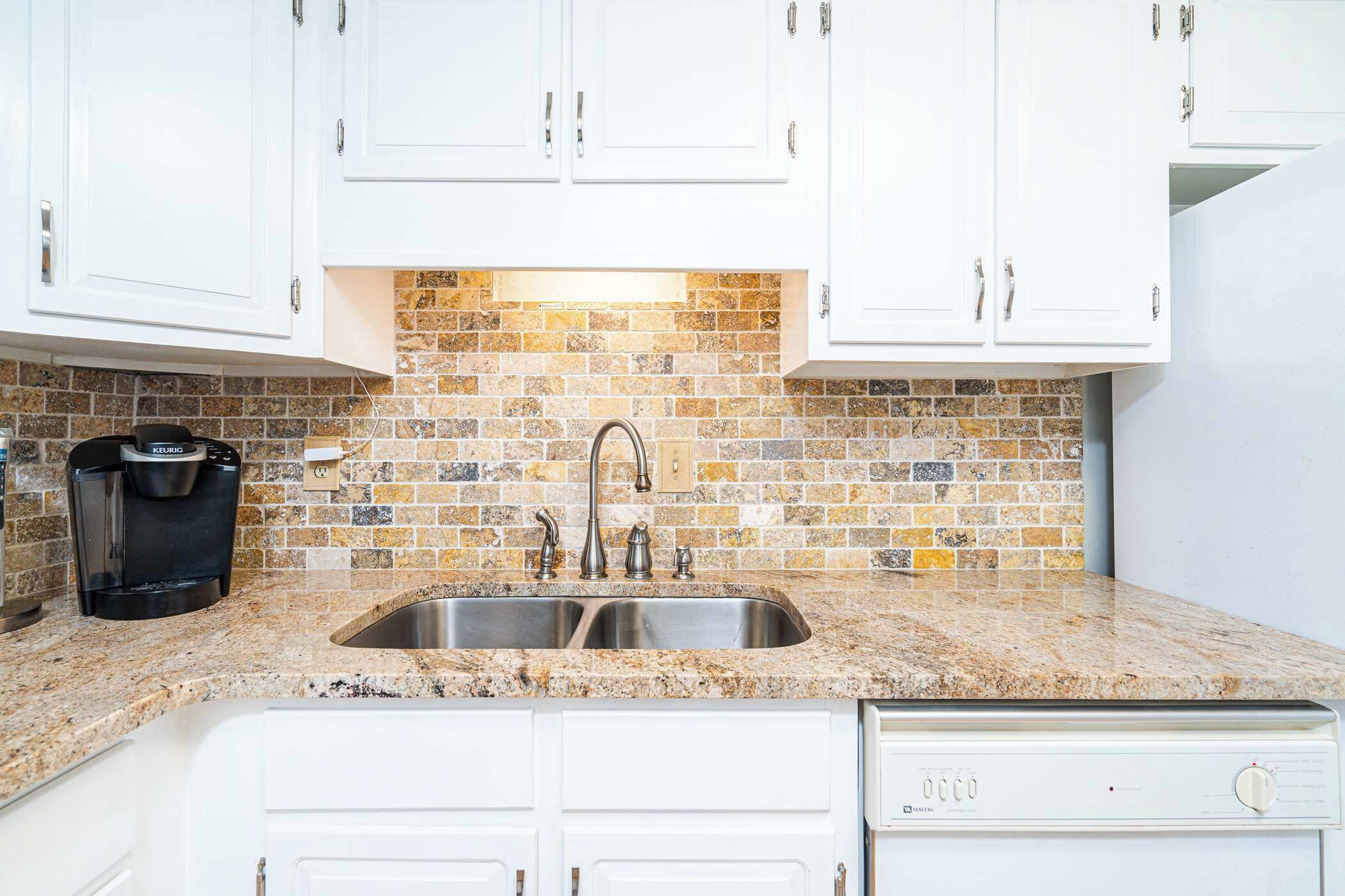 A kitchen with white cabinets, a granite countertop, a double sink, a coffee maker, and a dishwasher.