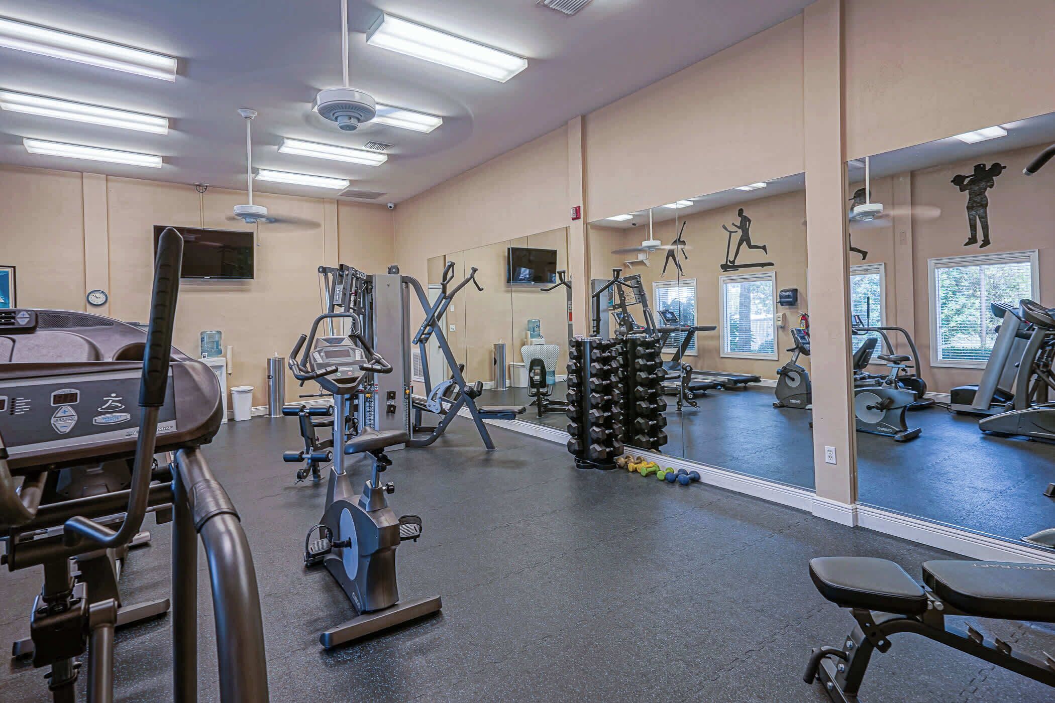 Ett gym med olika typer av träningsredskap, en stor spegel och en takfläkt.