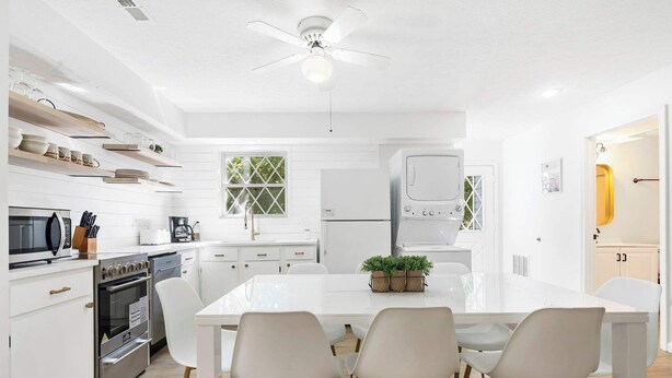 A modern kitchen with white cabinetry, a central island with chairs, and a ceiling fan. - Mystic Woods Trio Branson (Branson)