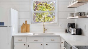 A modern kitchen with white cabinetry, a double sink, a window with a diamond-patterned view, and a coffee maker. - Mystic Woods Trio Branson (Branson)