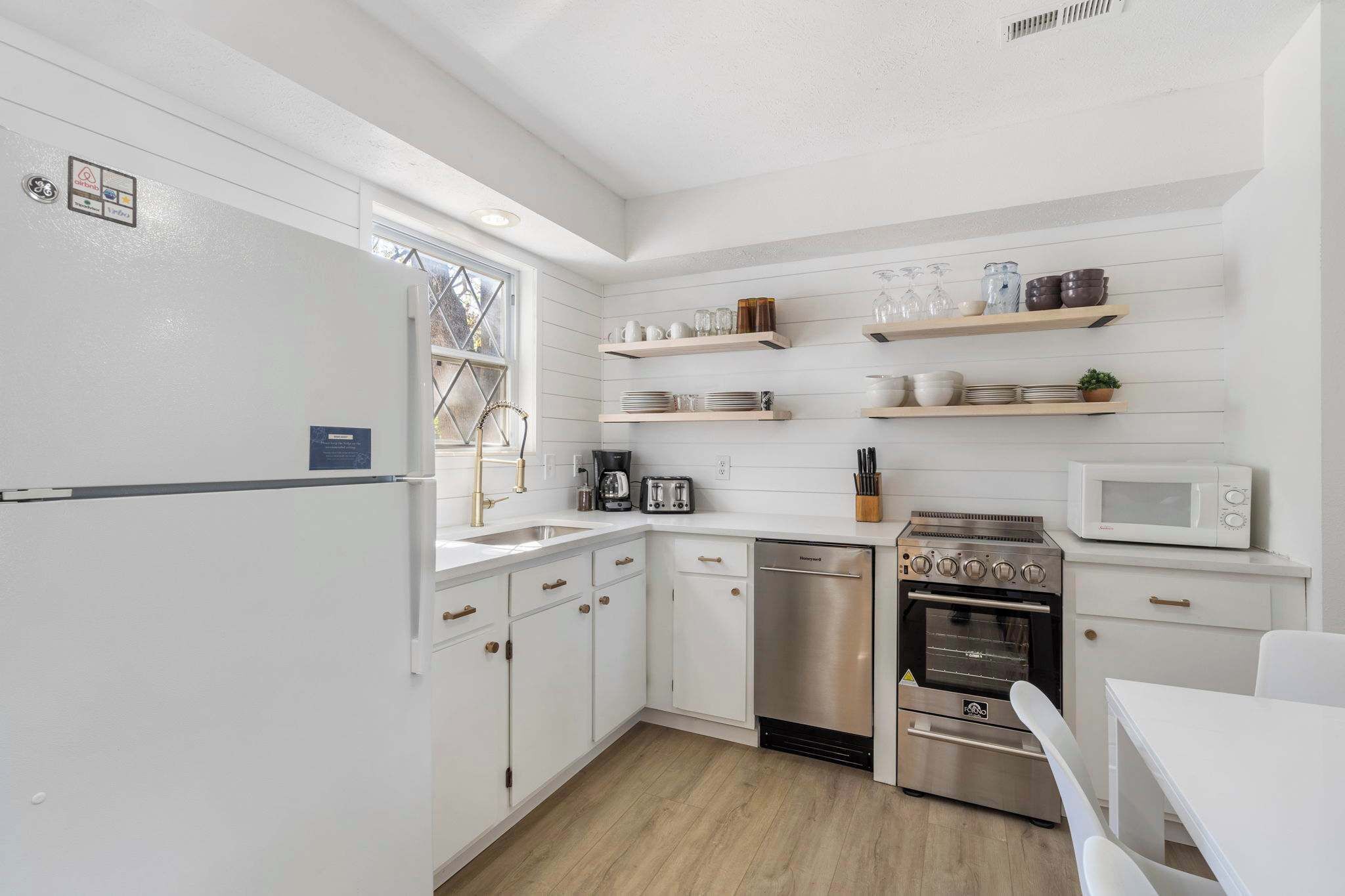 A modern kitchen with white cabinetry, stainless steel appliances, and wooden shelves.