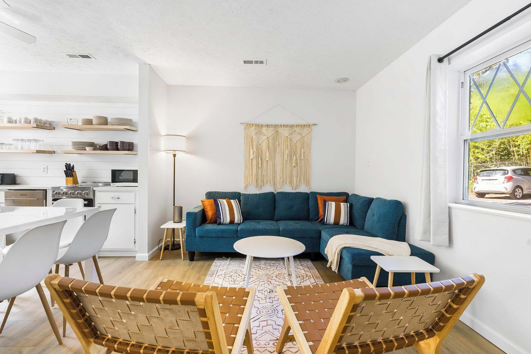 A modern living room with a blue sofa, a dining area with white chairs, and a kitchen in the background.