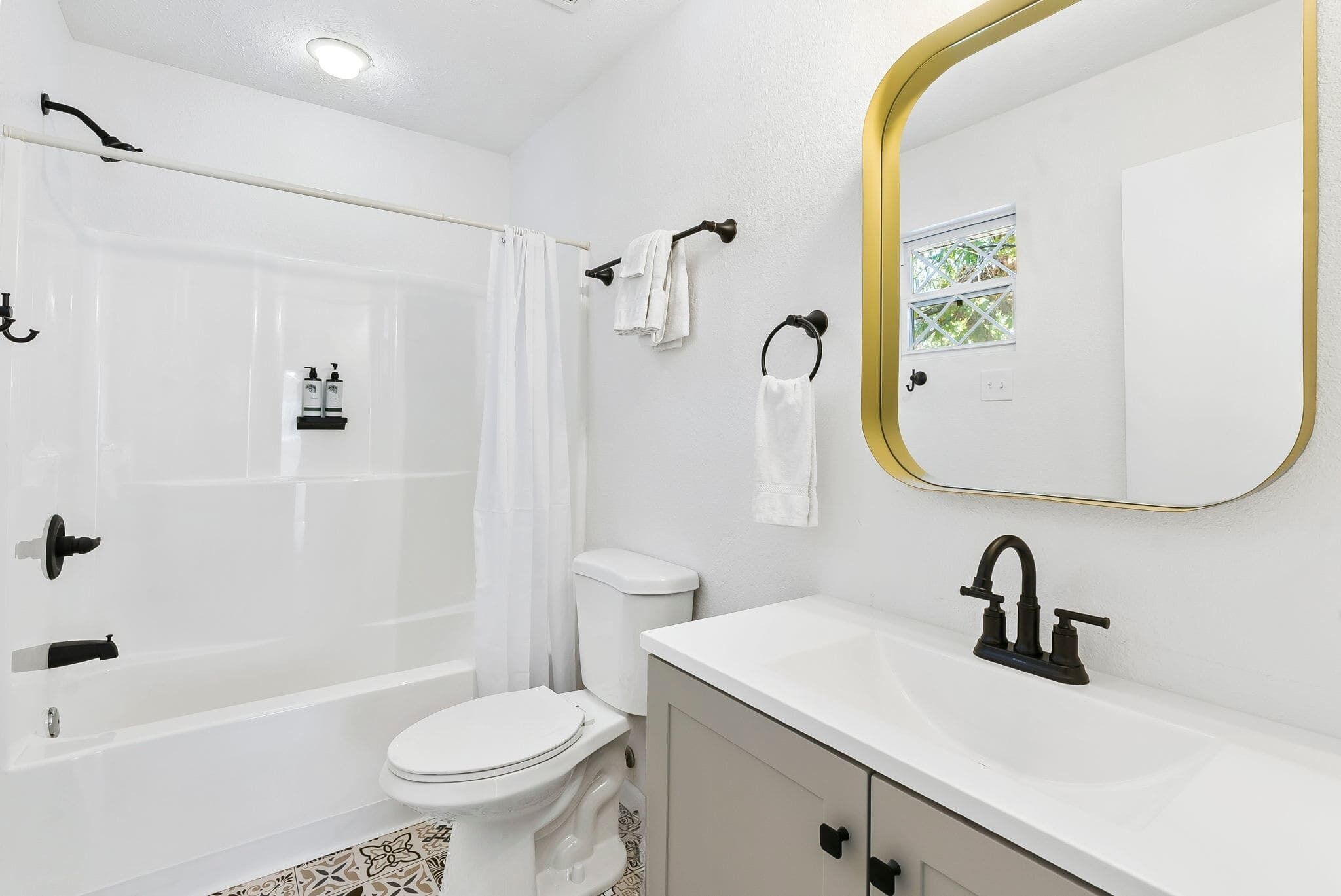 A bathroom with a bathtub, toilet, sink, and a mirror with a gold frame.