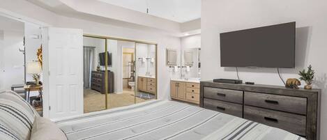 A bedroom with a large bed, a wardrobe, a TV, and a ceiling fan.