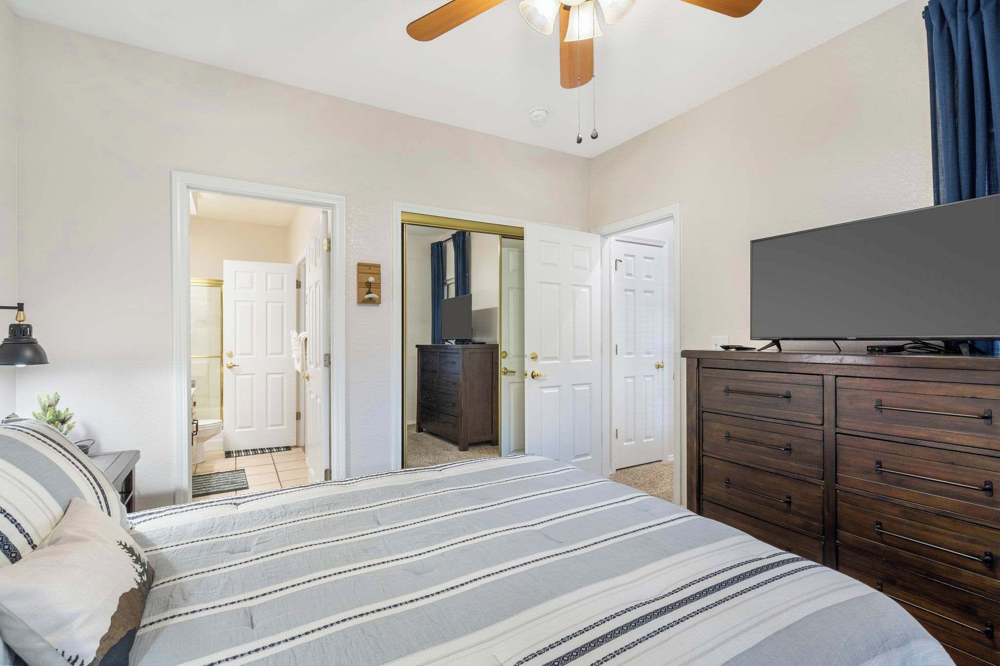 Une chambre à coucher avec un lit, une commode, un téléviseur et un ventilateur de plafond.