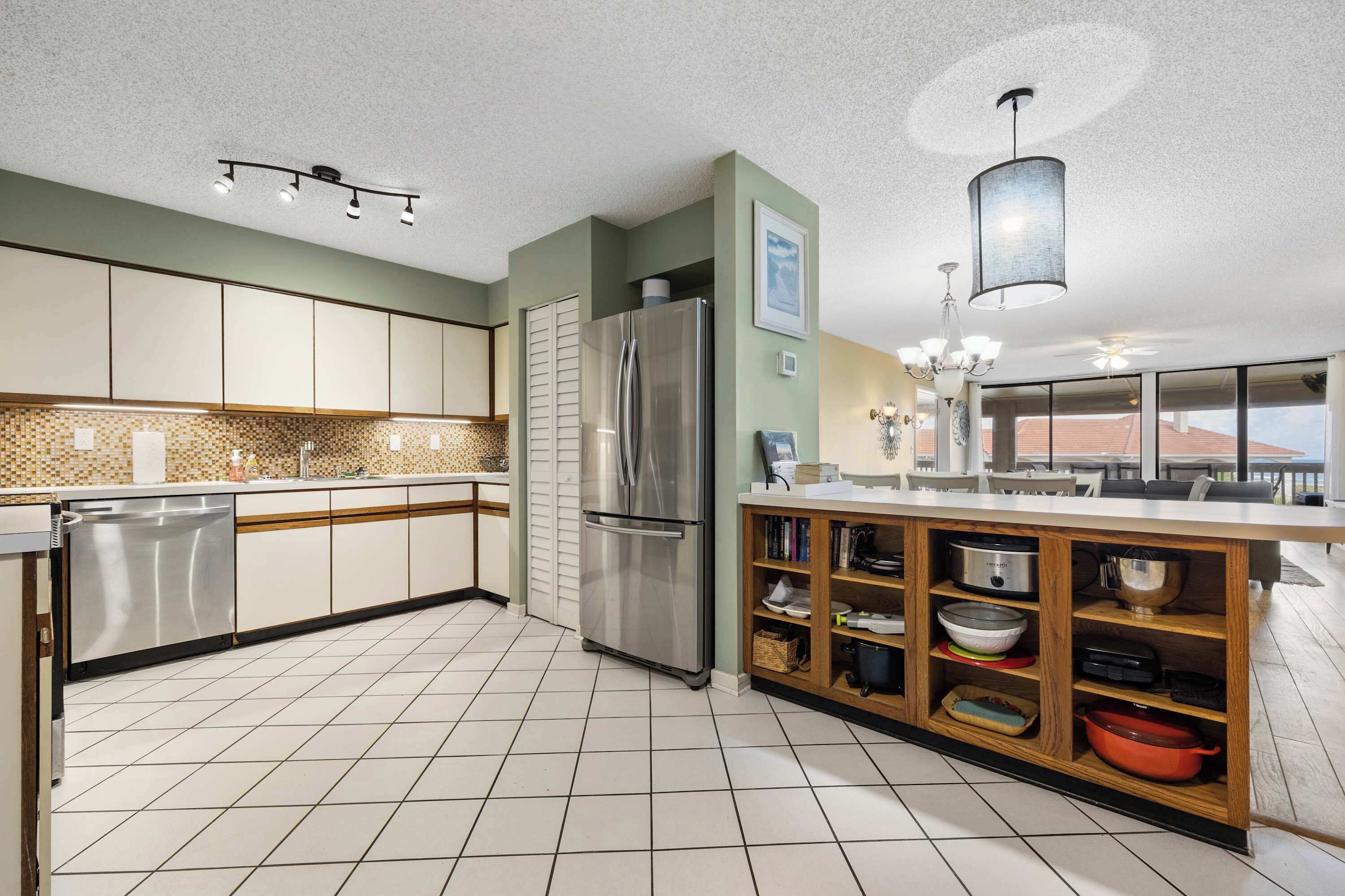 A modern kitchen with a stainless steel refrigerator, a wooden island with shelves, and a tiled backsplash.