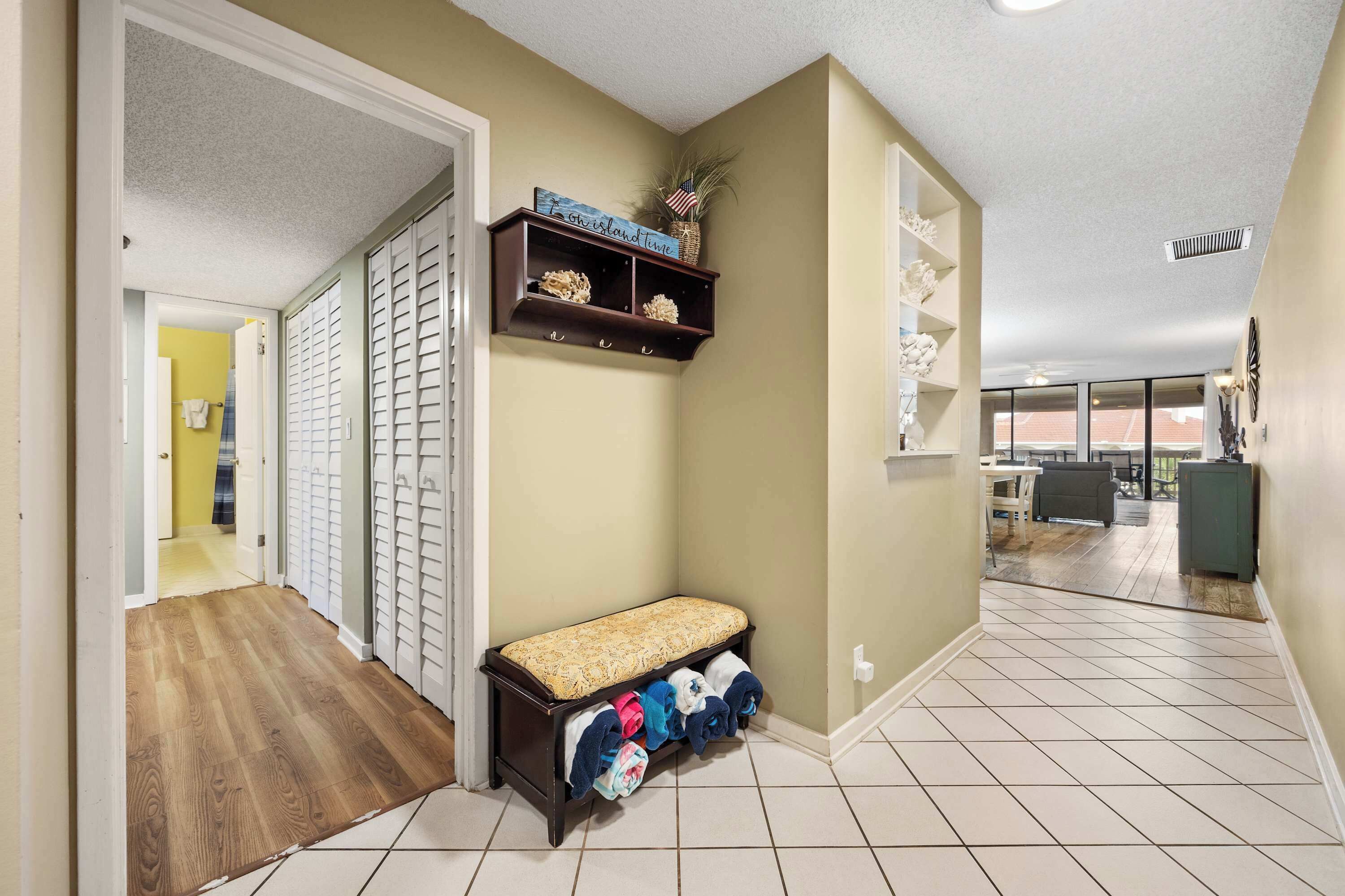 A hallway with a bench, a shelf with decorative items, and a view into another room.