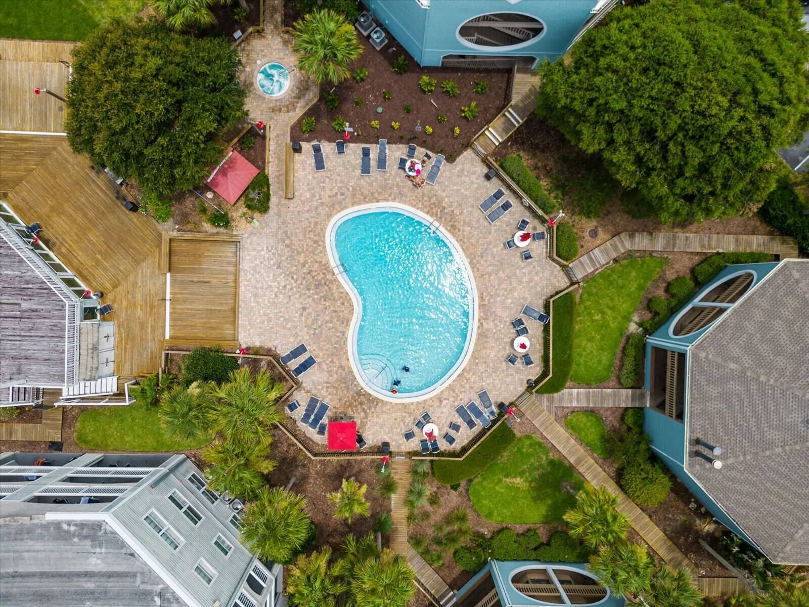 An aerial view of a residential property with a swimming pool surrounded by lounge chairs and a hot tub.