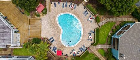 An aerial view of a residential property with a swimming pool surrounded by lounge chairs and a hot tub.