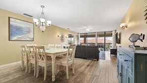 Spiseområde med et bord, stole, en lysekrone og et maleri på væggen.