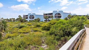 Et kysthotel med et karakteristisk, cirkulært altandesign, omgivet af frodig vegetation og en træpromenade.