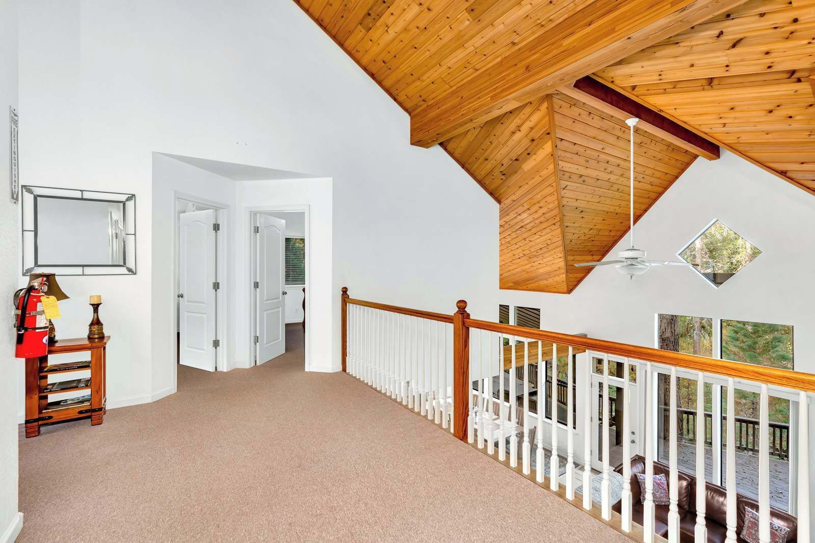 A spacious hallway with a wooden ceiling, white walls, and a white railing leading to a balcony.