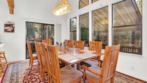 Un comedor con mesa y sillas de madera, ventanas grandes y una lámpara colgante.