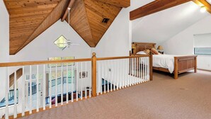 Un dormitorio con techo de madera, una cama, una mesita de noche y una ventana.
