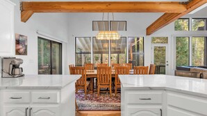 Una cocina moderna con armarios blancos, techo de madera y un comedor con una mesa grande y sillas.