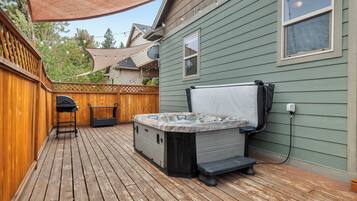 Eine Holzterrasse mit Whirlpool, Grill und überdachter Lounge-Ecke.