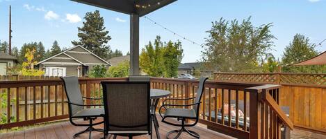 Una terraza de madera con mobiliario exterior, una zona cubierta y vistas a casas cercanas.