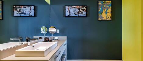 A modern bathroom with two sinks, a mirror, and three abstract paintings on the walls.