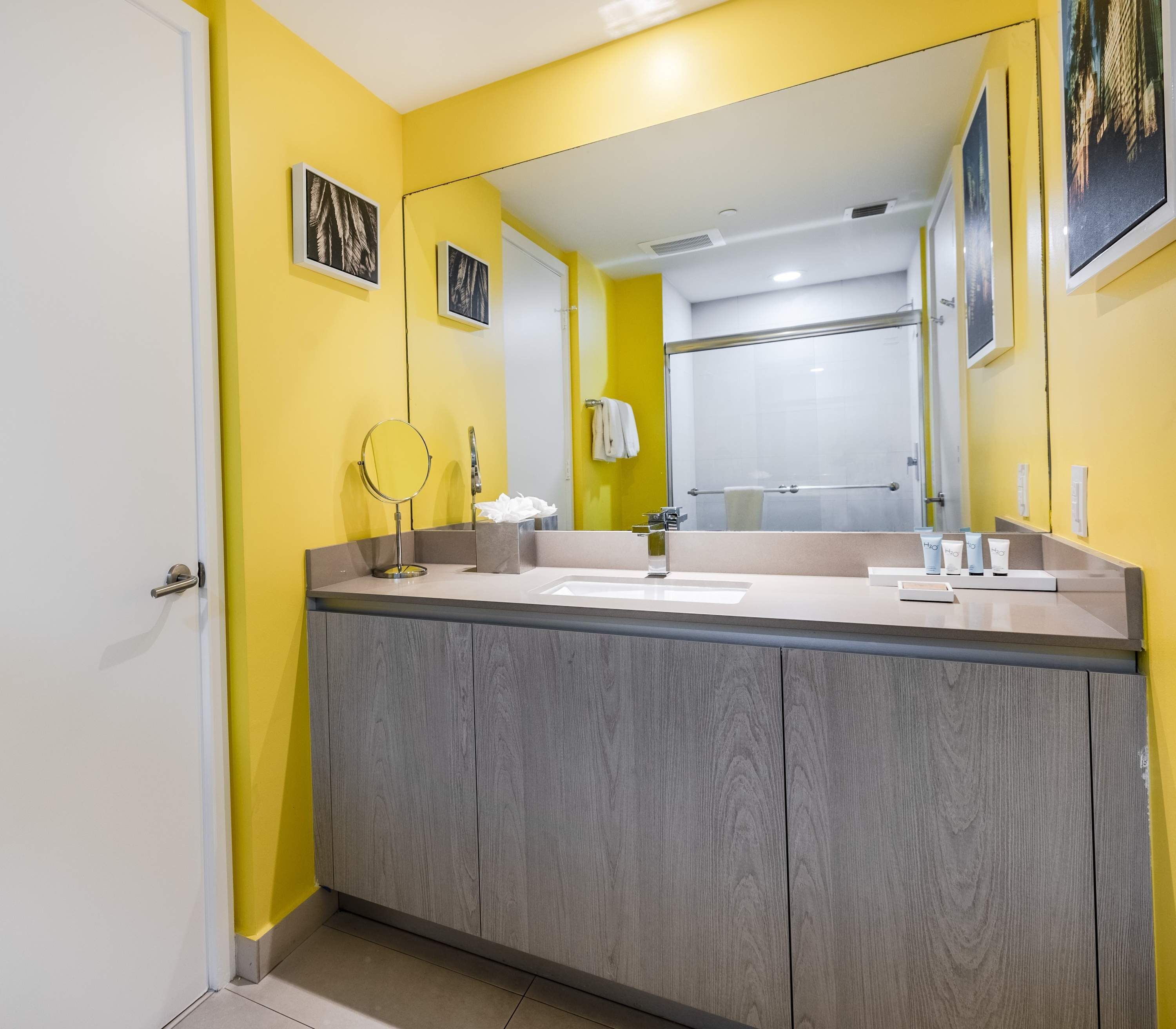 A bathroom with a wooden vanity, a large mirror, and a yellow wall.