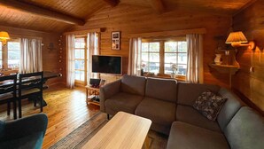 A cozy wooden interior with a sofa, TV, dining table, and chairs.