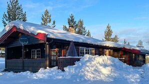 A wooden cabin with a snow-covered roof, surrounded by trees.