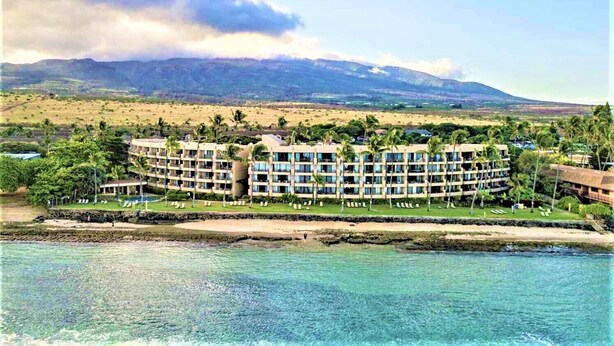 Een resort met meerdere gebouwen, een strand en een berg op de achtergrond.