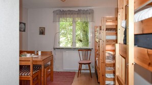 A cozy room with a wooden dining table, a chair, a window with a view of greenery, and a bunk bed structure.